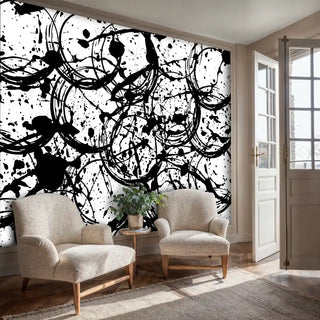 Abstract expressionist wall mural featuring dynamic black paint circles and splashes, displayed in living room with beige chairs