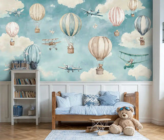 Adventure sky wallpaper featuring hot air balloons and vintage airplanes in soft blue and beige tones, displayed in a cozy children's bedroom with wooden bed and blue striped bedding