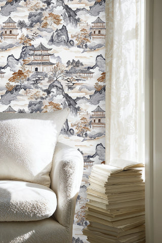 Asian landscape wallpaper with ink wash temples and autumn foliage beside a white armchair and stacked books