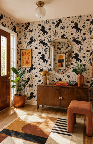Black and beige folk art wallpaper with horses and stars, in an entryway with gold mirror and walnut console