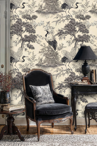 Black and cream crane toile wallpaper with blossoms and lake scene, in a classic room with velvet armchair