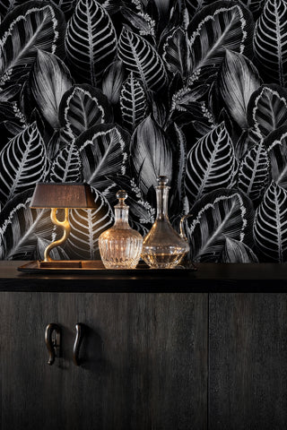Black and white botanical leaf wallpaper with detailed veining, above a dark credenza with crystal decanters