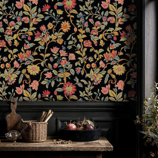 Black floral tapestry wallpaper with vibrant wildflowers and trailing vines, displayed in a rustic kitchen with wicker basket and fruit bowl