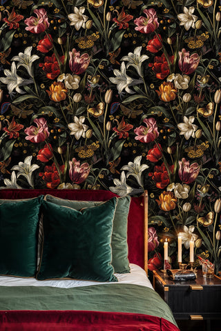 Black floral wallpaper with red tulips and white lilies, behind a bed with green velvet pillows and candles