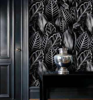 Black tropical foliage wallpaper with silver highlights, beside dark paneled door and mercury glass vase