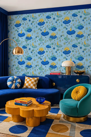 Blue and gold celestial cloud wallpaper with moons and stars in a living room with curved sofa and arc lamp