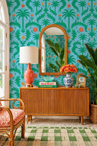 Blue and green tropical damask wallpaper with wildflowers, displayed in an entryway with arched rattan mirror