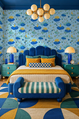 Blue cloud and gold sun celestial wallpaper in a bedroom with scalloped velvet headboard and globe chandelier