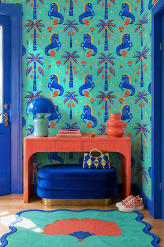 Blue rearing horses wallpaper with palm trees and stars in a colorful entryway with coral console and blue ottoman