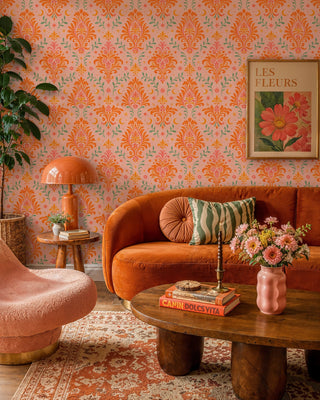 Blush damask wallpaper with ornate orange florals and stars, in a boho living room with curved orange sofa