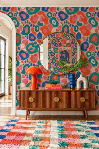 Bold abstract pattern wallpaper in teal and orange tones in an entryway with large gold round mirror and credenza