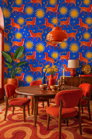 Bold blue wallpaper with red wildcats and gold suns, in a retro dining room with orange pendant light