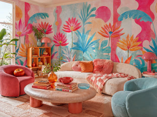 Bold pink and teal floral wall mural with abstract shapes in a cozy living room with curved beige sofa