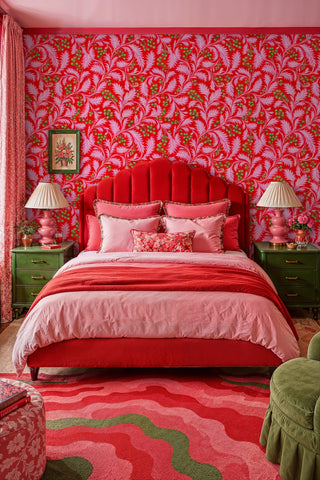Bold red botanical wallpaper with curling pink leaves and berries behind a velvet scalloped headboard