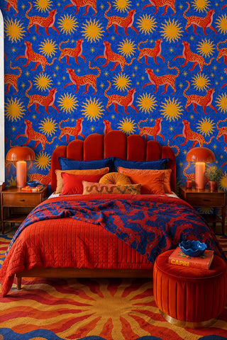 Bold wildcat and sun wallpaper in blue and red, behind a velvet scalloped headboard in a vibrant bedroom