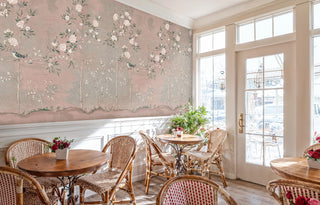 Botanical chinoiserie wall mural with delicate birds and peonies, featured in bright cafe dining space with wicker chairs