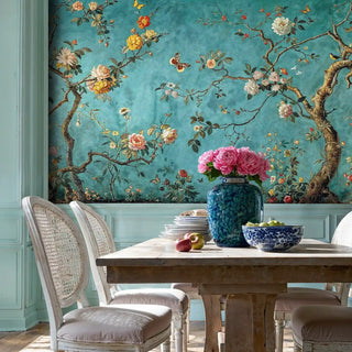 Botanical chinoiserie wallpaper featuring blooming branches on teal background, shown in refined dining room with cane chairs