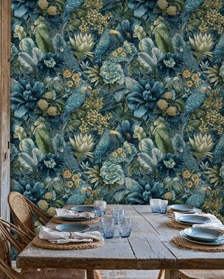 Botanical parrot wallpaper in deep teal and green behind a rustic farmhouse table with woven placemats and blue glassware