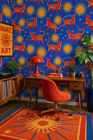 Celestial cat wallpaper with golden sunbursts on cobalt blue, in a creative home office with vinyl shelf