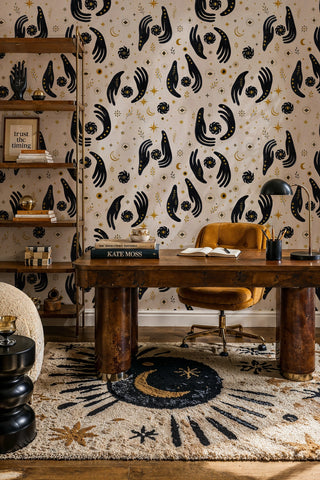 Celestial evil eye wallpaper with dark hands and gold accents in a home office with wooden desk and moon rug