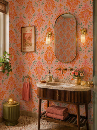 Celestial floral damask wallpaper in orange and blush, in a powder room with wood vanity and brass sconces