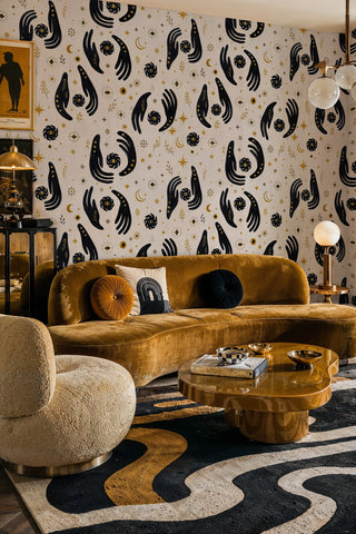 Celestial hands and evil eye wallpaper with gold stars on beige in a living room with curved velvet sofa