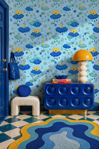 Celestial wallpaper with blue clouds, gold suns, and moons in a bold entryway with blue cabinet and wave rug