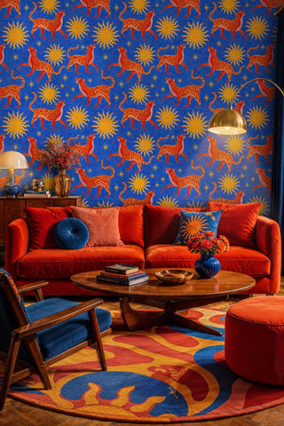 Celestial wildcat wallpaper with red cats and golden suns on blue, in a bold living room with orange sofa