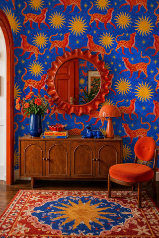 Celestial wildcat wallpaper with suns and stars on blue, in an entryway with wavy round mirror and credenza