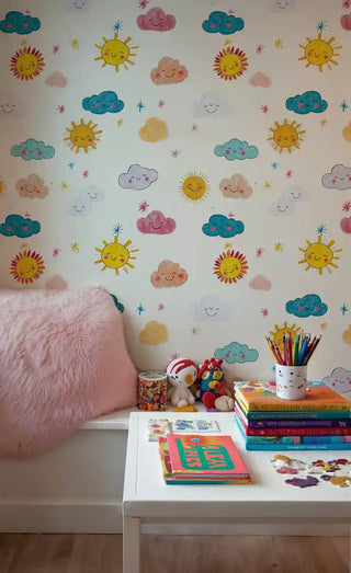 Cheerful sun and cloud wallpaper featuring colorful hand-drawn elements, shown in kids room with pink chair and books