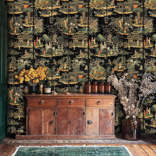Chinese pavilion wallpaper in black and gold, shown in rustic room with wooden sideboard