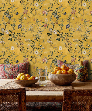 Chinoiserie floral wallpaper on gold background with trailing vines, in a bohemian dining area with citrus bowls and cushions