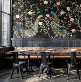 Chinoiserie wall mural featuring peacocks and blush florals on dark ground, in an industrial cafe with rustic wood table