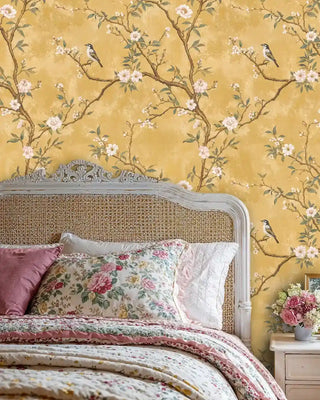 Chinoiserie wallpaper with birds and flowering branches, shown in romantic bedroom with cane headboard and floral bedding