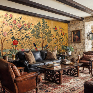 Classic chinoiserie wallpaper featuring birds among flowering trees, shown in rustic living room with stone wall