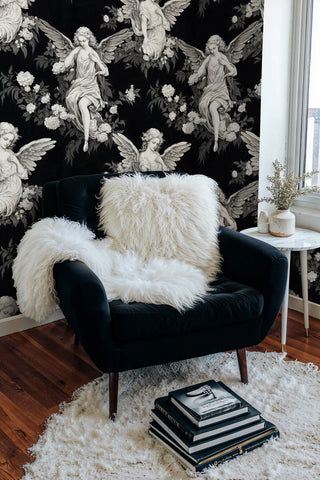 Classical angel wallpaper with botanical elements, shown in living room with navy armchair and white fur throw