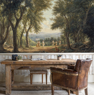 Classical pastoral wall mural featuring ancient trees and dancing figures in earth tones, shown in rustic study with wooden desk