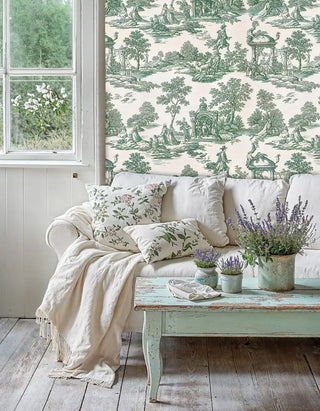 Classical toile wallpaper showing garden scenes in sage green, featured in cottage living room with floral pillows