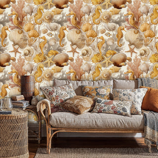 Coastal seahorse wallpaper in gold tones shown in cozy living room with neutral sofa and patterned pillows