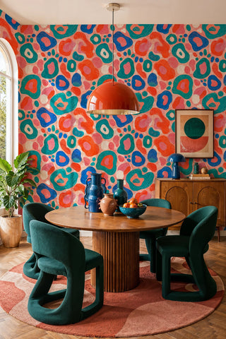Colorful abstract blob pattern wallpaper in pink and teal shown in a dining room with orange dome pendant light