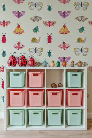 Colorful insect wallpaper featuring butterflies and beetles shown in organized playroom with storage cubbies