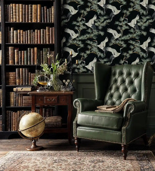 Crane and pine wallpaper in black and green with detailed birds, displayed in classic study with leather armchair and antique globe