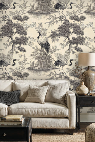 Cream and black crane toile wallpaper with pine trees and blossoms, in a living room with linen sofa and lamp