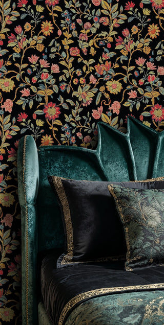 Dark botanical embroidery wallpaper with lush florals on black, behind a teal velvet wingback chair with decorative cushions