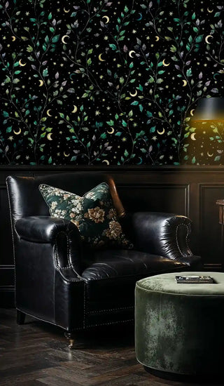Dark botanical wallpaper featuring celestial motifs, shown in classic library with leather armchair and ottoman