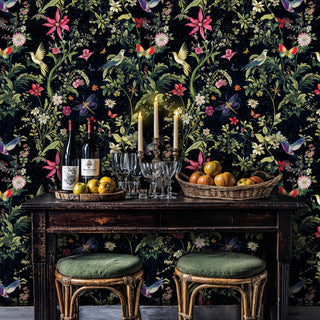 Dark botanical wallpaper featuring colorful birds and pink flowers, displayed in dining room with wooden table and candles