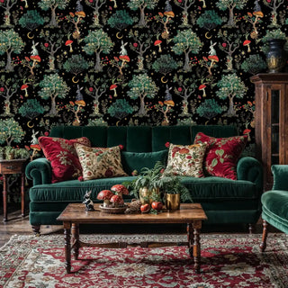 Dark botanical wallpaper featuring whimsical woodland scenes in a luxurious living room with emerald velvet sofa