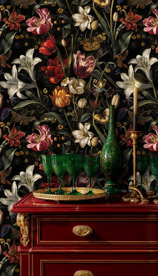 Dark botanical wallpaper with vivid flowers and butterflies on black, beside a red cabinet with green glassware