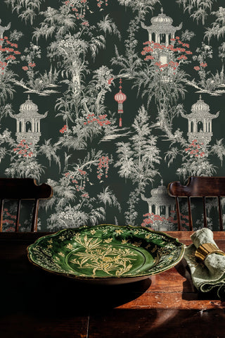 Dark chinoiserie garden wallpaper with red flowers and palm trees, shown with a green ceramic plate on table