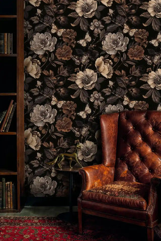 Dark floral butterfly wallpaper with sepia blooms on black background, shown in classic study with leather chair